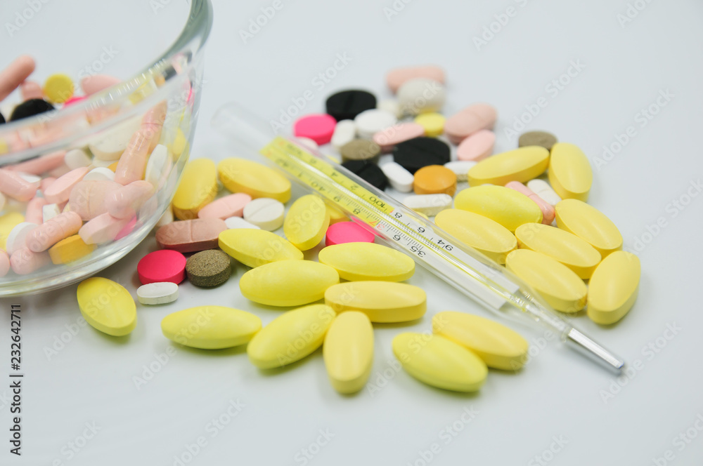 Assorted pharmaceutical medicine pills, tablets and capsules with thermometer on glass bowl