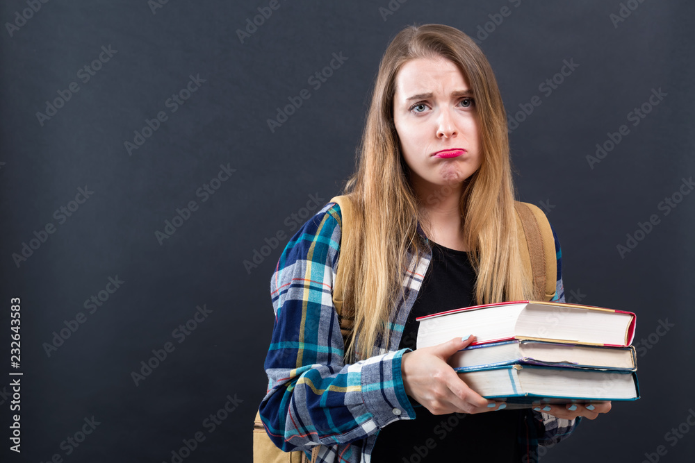 Sad young student with pile of textbooks on a black background Sad young student with pile of textbooks on a black background