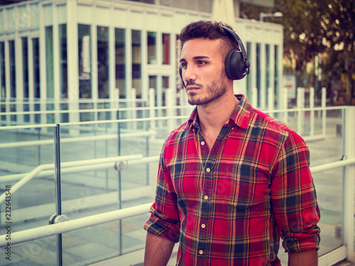 Young attractive man in city setting listening to music with headphones, walking