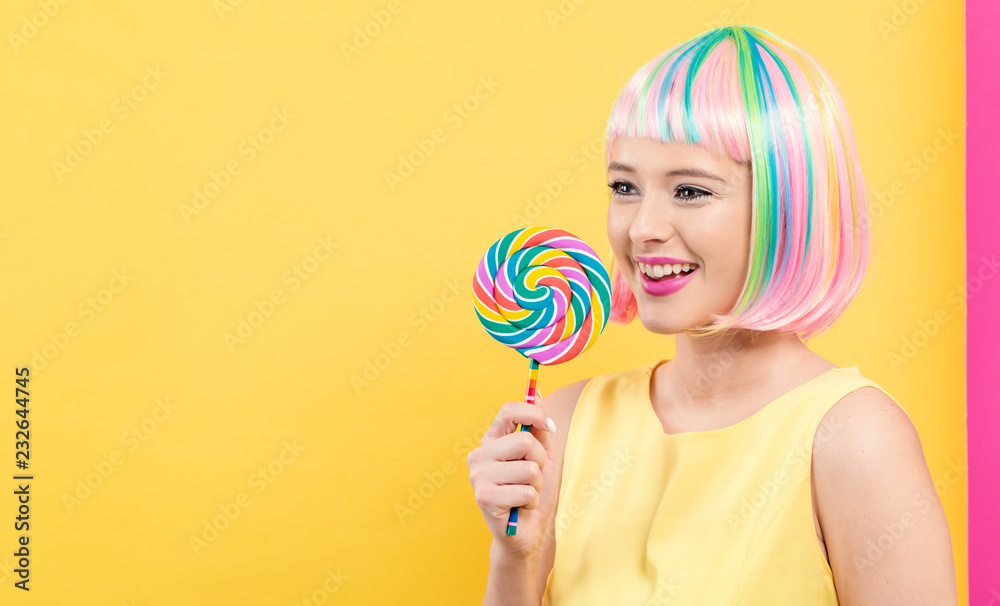 Woman in a colorful wig with a giant lollipop on a split yellow and pink background