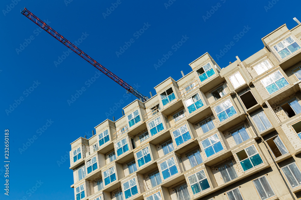 Tower crane and unfinished building an apartment house on a background of blue sky