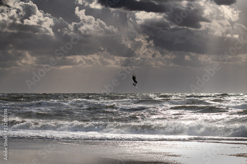 Silhouette of a jumping kitesurfer with sun coming through clouds
