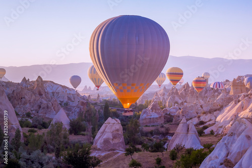 Hot air balloons flying in beautiful Cappadocia hilly landscape, amazing tourism attraction in Goreme, Anatolia, Turkey, morning sun light