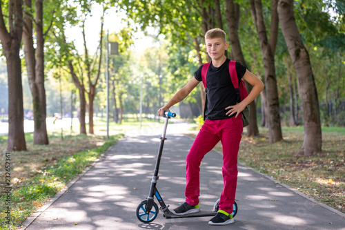 outdoor portrait of young happy preteen boy riding a scooter on natural background