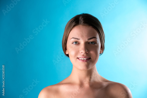 Beautiful Woman Face. Beauty Portrait of young woman brunette smiling on blue background. Perfect Fresh Skin. Youth and Skin Care Concept.