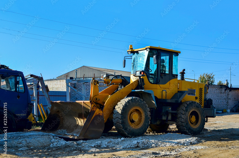 Yellow excavator on the construction site is preparing to load the soil into the dump truck. Wheel loader with iron bucket Yellow excavator on the construction site is preparing to load the soil into the dump truck. Wheel loader with iron bucket