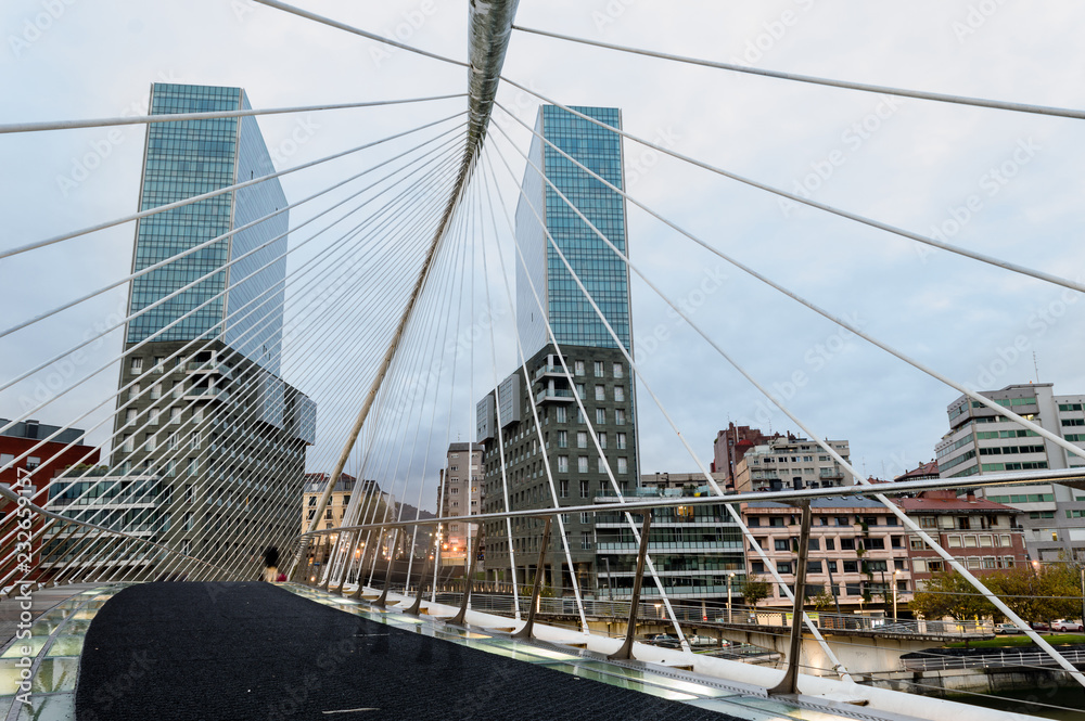 Obraz premium View of a Zubizuri bridge,over the Nervion River, in a cloud day, between the towers of Bilbao, Vizcaya, Spain.