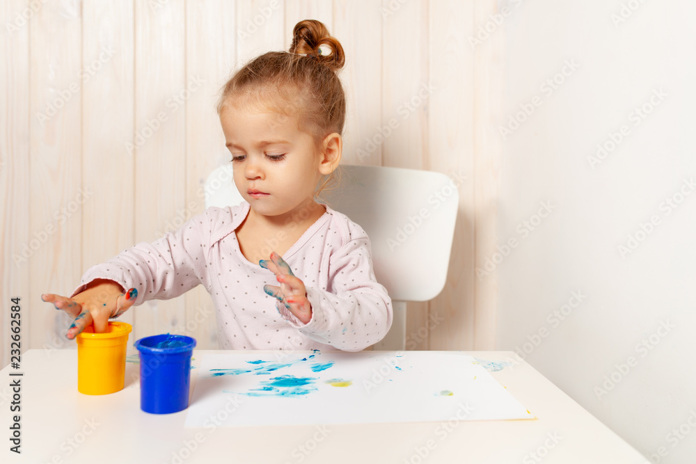 Beautiful little girl draws with finger paints on a white sheet of paper. Creative child development in kindergarten or free time at home Beautiful little girl draws with finger paints on a white sheet of paper. Creative child development in kindergarten or free time at home