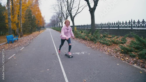 Young pretty beautiful blond hipster woman in pink windstopper having fun riding skateboard longboard downhill on beautiful road in slow motion photo