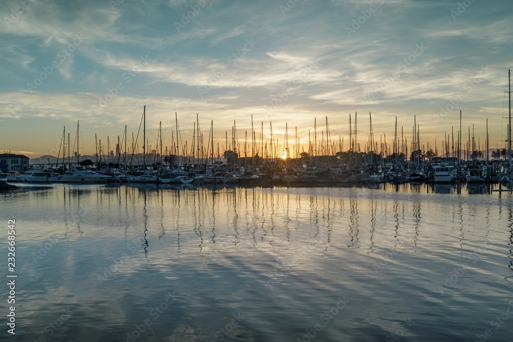 Sun setting on Emeryville Marina. Sailboats moored in San Francisco Bay with sunset skies and water reflections. Alameda County, California, USA.