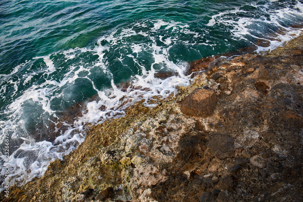 Aerial top view of sea waves hitting rocks on the beach with turquoise sea water. Amazing rock cliff seascape in the coastline. Aerial view of sea waves and fantastic Rocky coast. Mediterranean Sea.