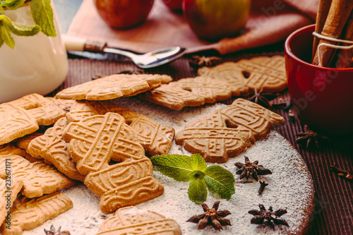 Speculaas Christmas cookies on a wooden board sprinkled with powdered sugar with mint leaves and oriental spices