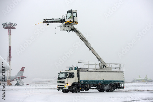 De-icing truck on the apron of international airport during snow blizzard