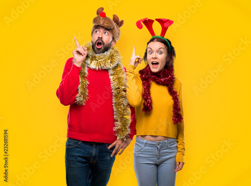 Couple dressed up for the christmas holidays intending to realizes the solution while lifting a finger up on yellow background