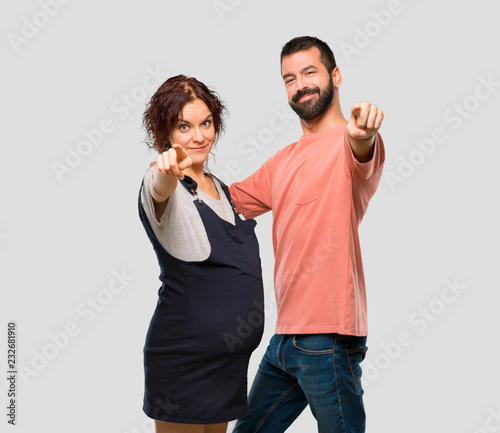 Couple with pregnant woman points finger at you with a confident expression on isolated grey background