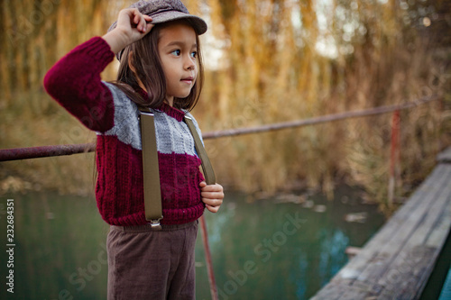 Child girl stands on wooden bridge on background of river.