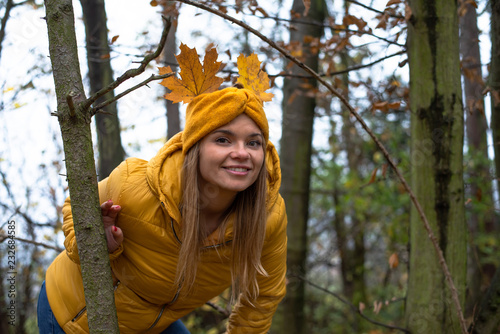 Beautiful young woman is having fun in the autumn forest with leaves on her hair