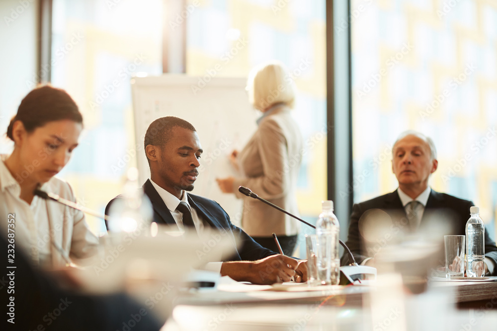 African-american delegate making working notes while sitting at conference among colleagues