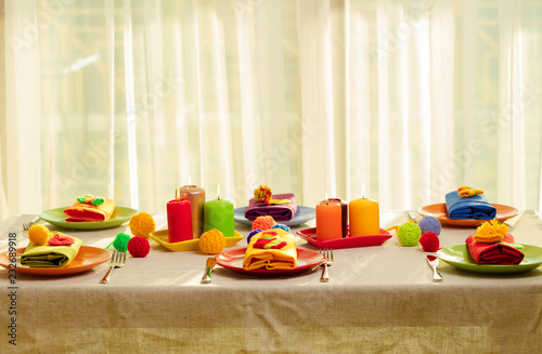 Multicolored plates and linen napkins with knitted decor. Table setting for the autumn or winter cold season - Thanksgiving, Halloween, Christmas and New Year.