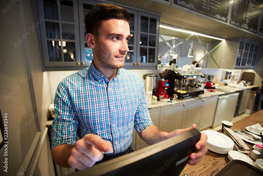 Young sales clerk standing by counter in front of computer and entering order information Young sales clerk standing by counter in front of computer and entering order information