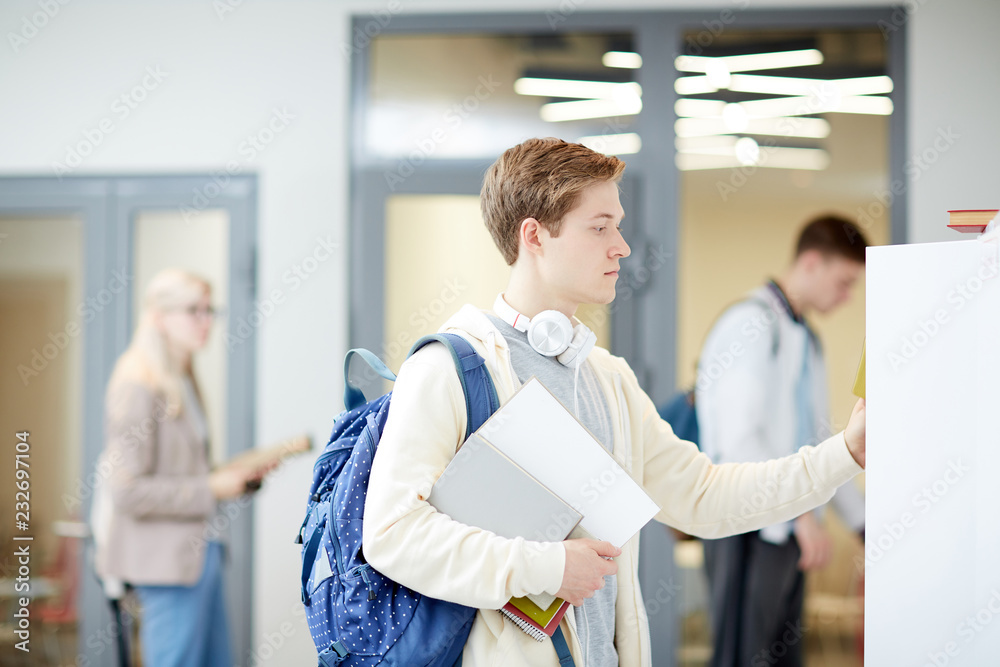 Fototapeta premium One of modern college students with backpack looking for book in library that can help him with home task