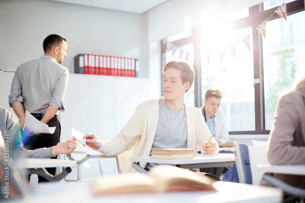 Casual guy passing over note with crib to his groupmate behind teacher back Casual guy passing over note with crib to his groupmate behind teacher back