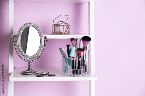 Organizer with makeup cosmetic products on shelf near color wall. Space for text