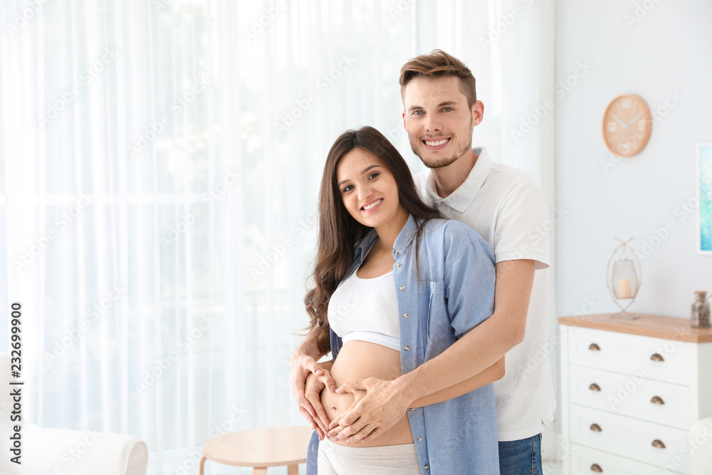Pregnant woman and her husband showing heart with hands at home. Space for text Pregnant woman and her husband showing heart with hands at home. Space for text