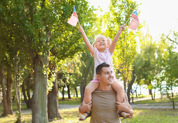 Man holding his daughter with American flags in park on sunny day