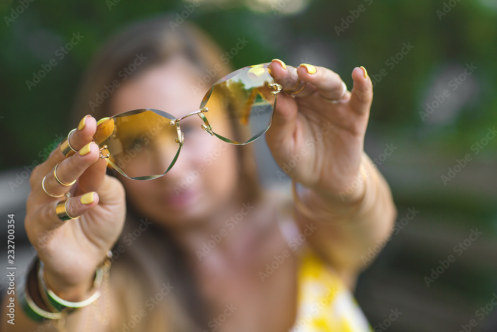 Young woman holding yellow sunglasses in her hands in front of camera. Still of stylish accessories Young woman holding yellow sunglasses in her hands in front of camera. Still of stylish accessories