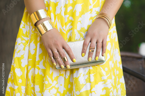 Unrecognizable woman holding wallet in her hands. Lady`s hands wearing rings and accessiories. Girl in yellow dress