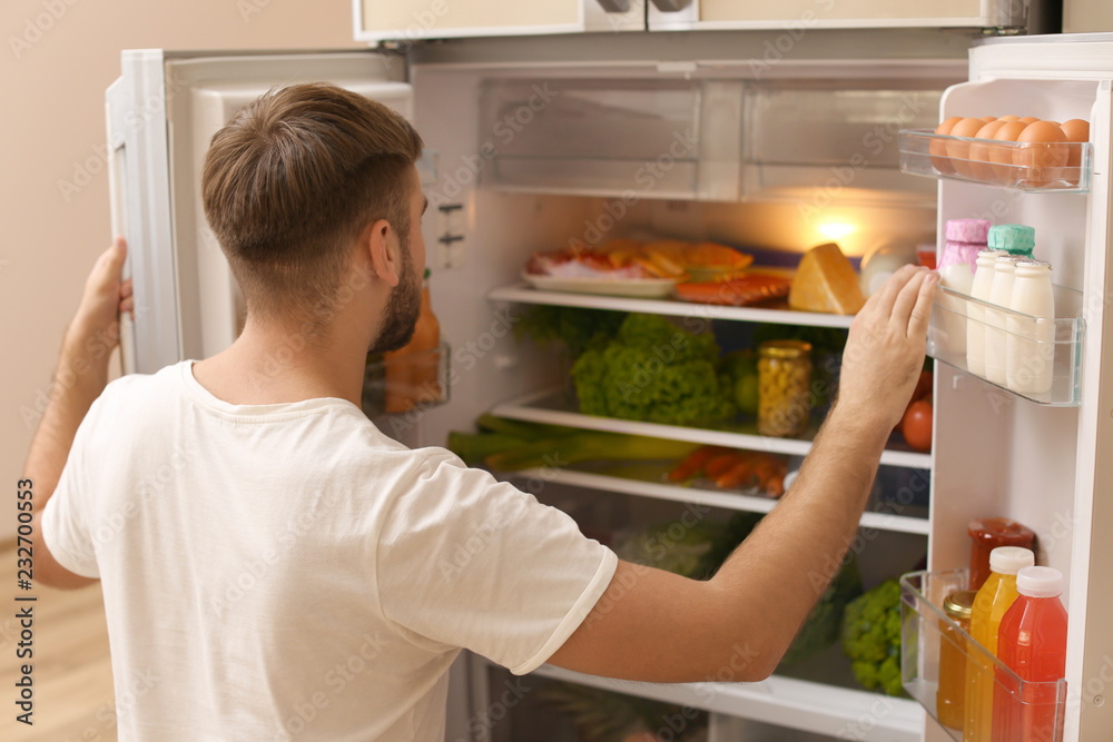 Young man choosing food in refrigerator at home