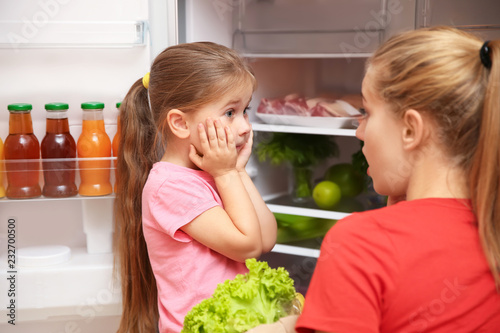 Emotional young mother and daughter near refrigerator at home