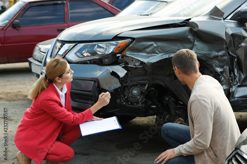 Man reporting and insurance agent filling claim form near broken car outdoors photo