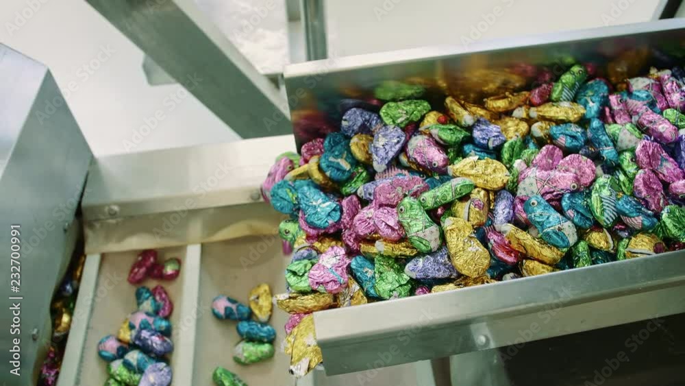 Candy factory. Bunch of wrapped candies falling from conveyor on packing containers in confectionery factory.