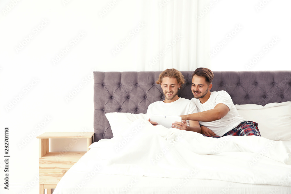 Fototapeta premium Happy gay couple with tablet computer on bed at home