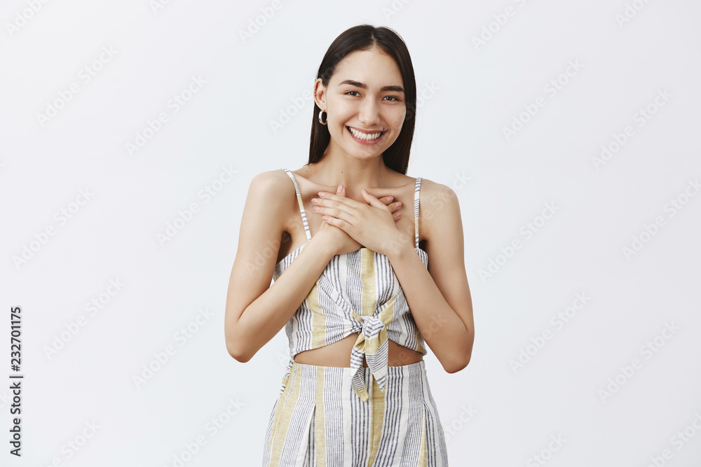 Portrait of charming asian girl touched to bottom of heart, smiling joyfully, holding palms on breast, being pleased with great compliments, standing over gray background Portrait of charming asian girl touched to bottom of heart, smiling joyfully, holding palms on breast, being pleased with great compliments, standing over gray background