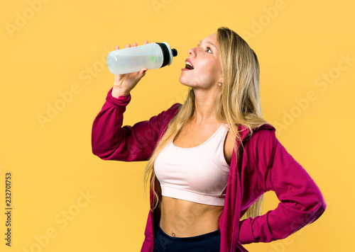 Pretty sport woman with a bottle of water on yellow background