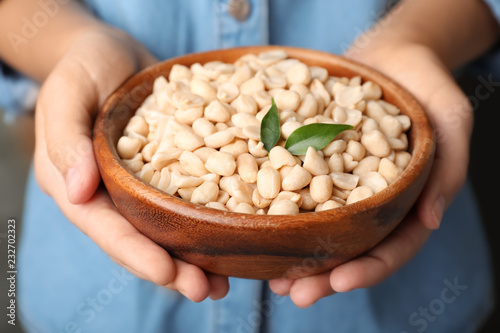 Woman holding bowl with shelled peanuts, closeup