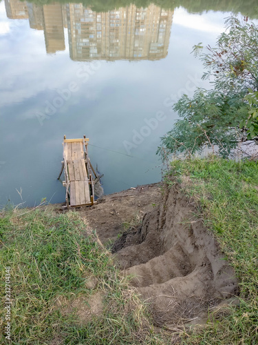 The bridge of pine boards on the bank of the river for fishing with a rod. Steps in the ground to the bridge