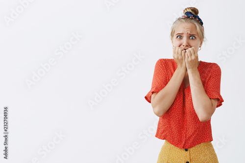 Woman freaking out seeing huge disgusting spider. Portrait of scared panicking cutie in headband and vintage red blouse with dottes, biting fingernails, grimacing and frowning from fear photo