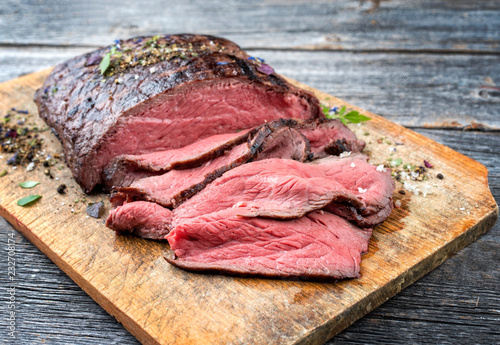 Traditional barbecue dry aged sliced roast beef steak with herbs as closeup on an old cutting board