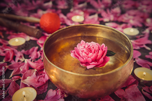 Tibetan singing bowl with floating inside in water pink peony flower. Burning candles, special sticks and petals on the black stone background. Meditation and Relax. Exotic massage. Selective focus. photo