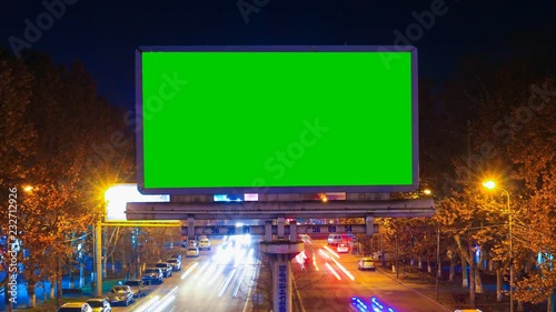 A billboard with green chroma key on a background of a city night landscape of fast moving cars with long exposure. Time Lapse video.
