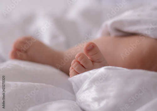 Baby sleeping in white bed, his sweet legs filled with the  tenderness of a mother's heart