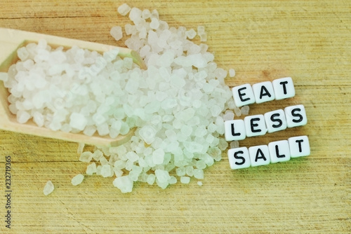 Eat less salt recommendation with plastic letters and granulated salt on wooden chopping board 