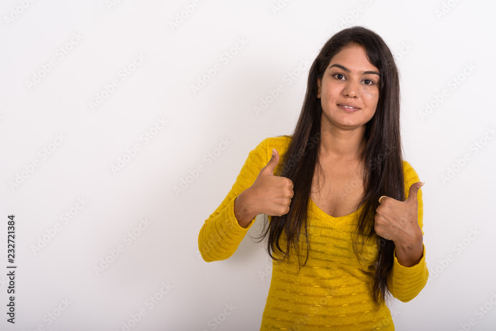 Studio shot of young happy Indian woman smiling while giving thu Studio shot of young happy Indian woman smiling while giving thu