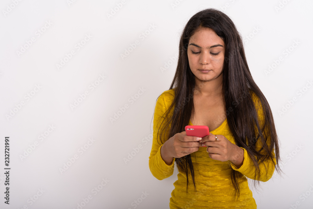 Studio shot of young Indian woman using mobile phone against whi Studio shot of young Indian woman using mobile phone against whi