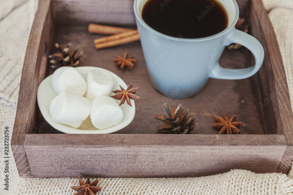 Naklejka premium Cup of coffee on rustic wooden tray, sweet marshmallow and warm woolen sweater. Cozy autumn or winter weekend or holidays at home. Fall home decoration with hot drink mug. Hygge morning style concept