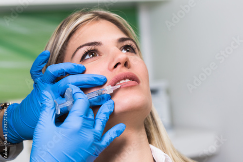 Beautiful young woman gets botox injection in her lips. Woman in beauty salon. Plastic surgery clinic.